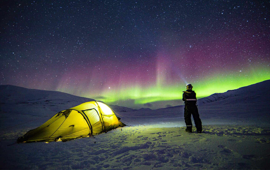 Homme qui regarde les aurores boréales à coté de sa tente