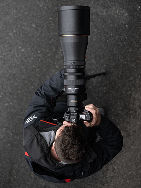 Un photographe sur le bitume avec un objectif 600mm noir Nikon